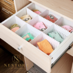 "Adjustable white drawer divider organizer holding folded clothes in wooden dresser drawer"